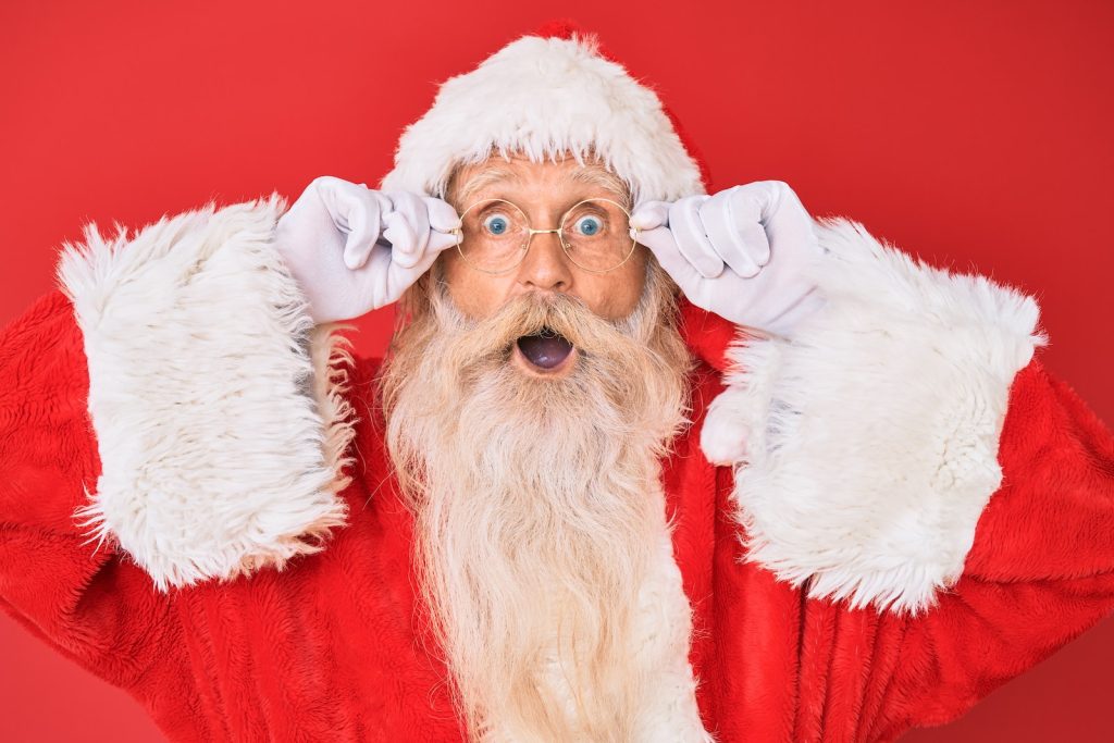 santa claus looks surprised with his glasses in front of a red wall