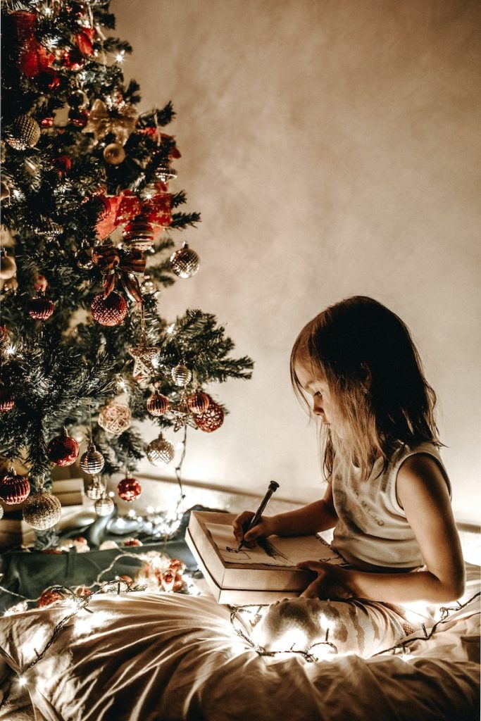 girl writing a letter for santa claus during christmas near a tree